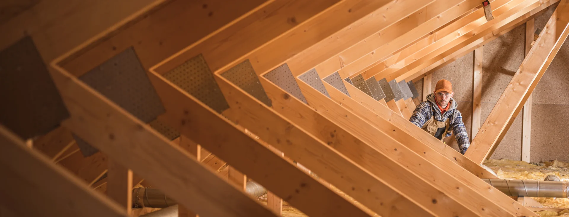 Worker wearing safety gear installing wooden roof trusses inside a building under construction.