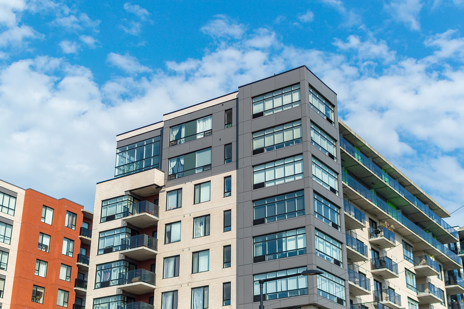 Modern multi-story apartment building with balconies under a partly cloudy sky.