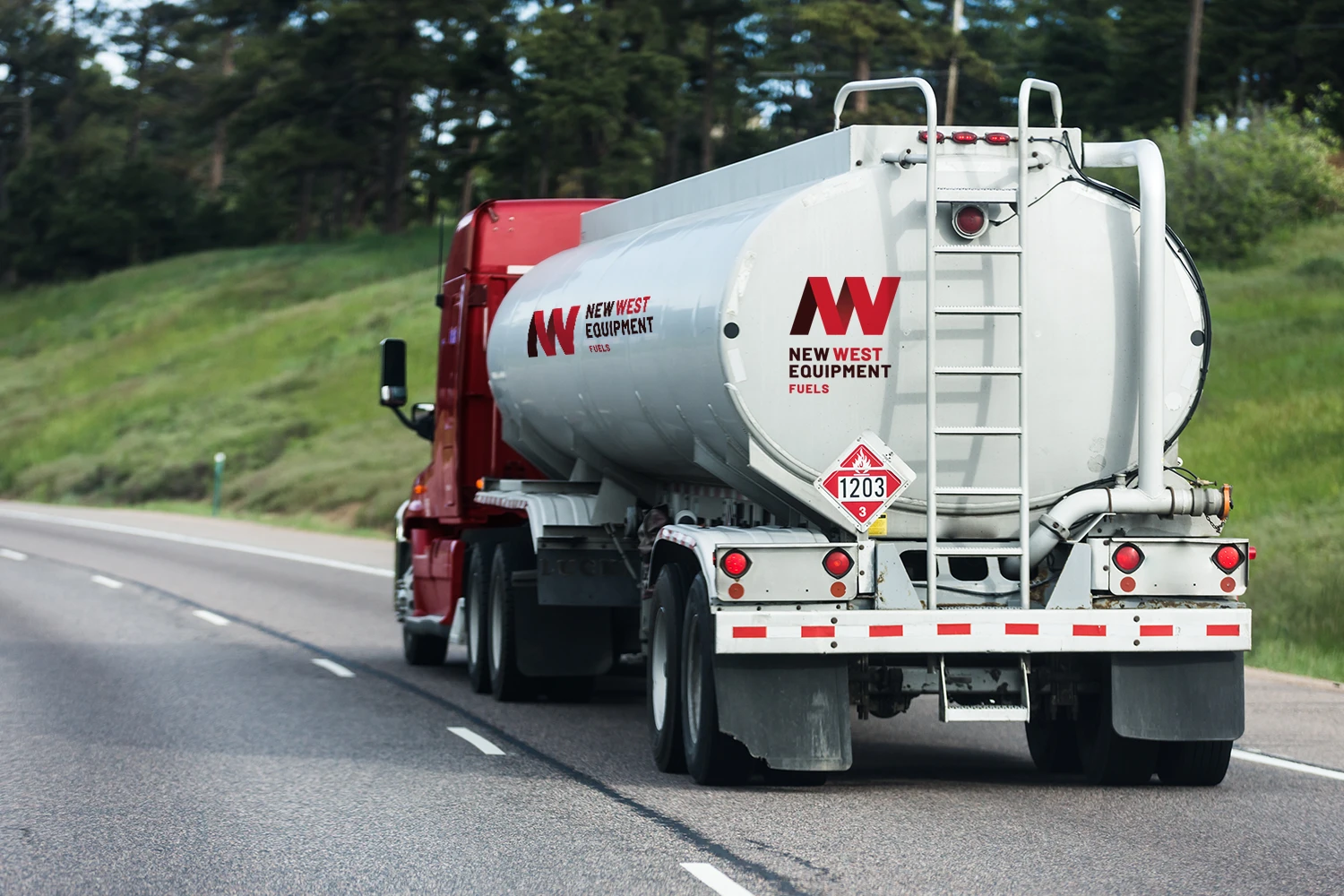 Red and white tanker truck labeled "New Way Transport" driving on a highway surrounded by greenery.