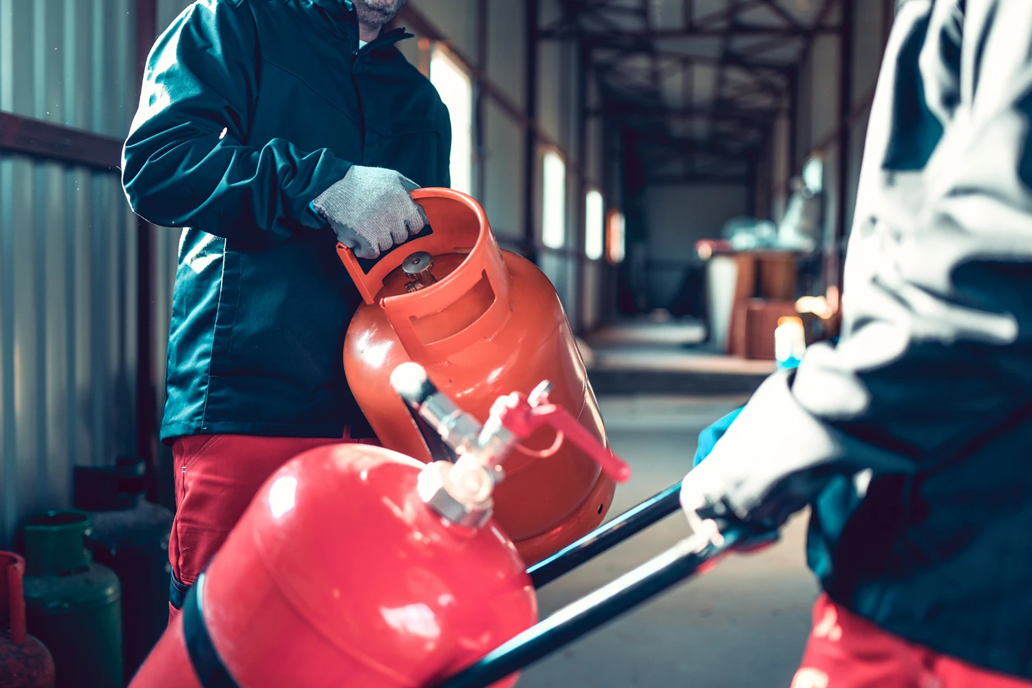 People wearing protective gloves refilling a red fire extinguisher with a gas cylinder in an industrial setting.