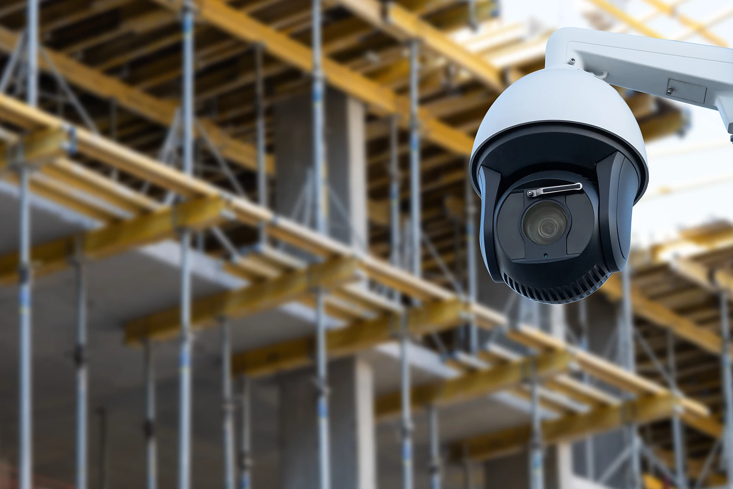 White security camera mounted outdoors with a construction site background featuring scaffolding and metal beams.