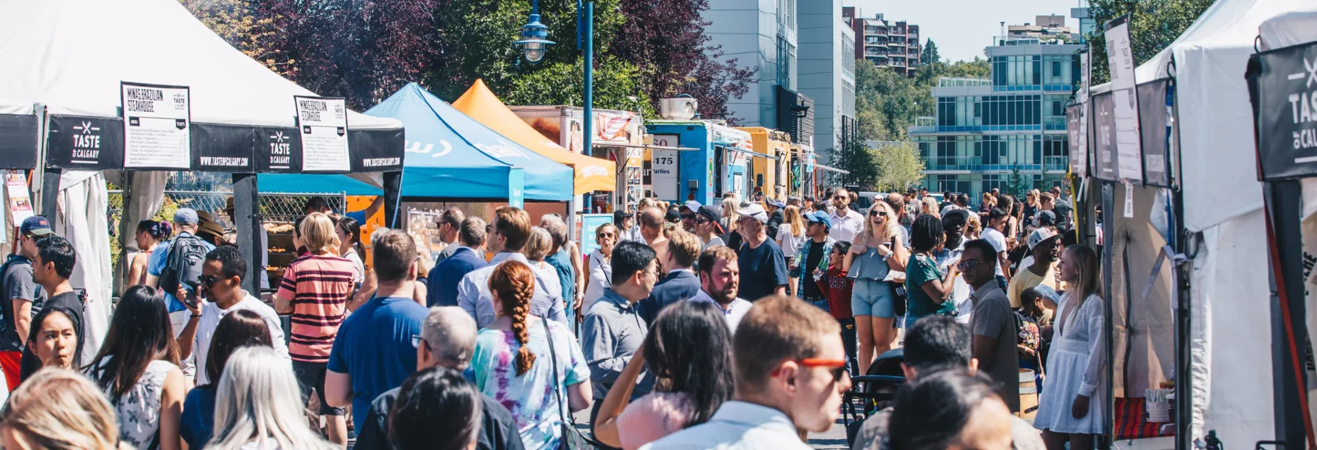 Crowd of people browsing outdoor market stalls on a sunny day in an urban area.