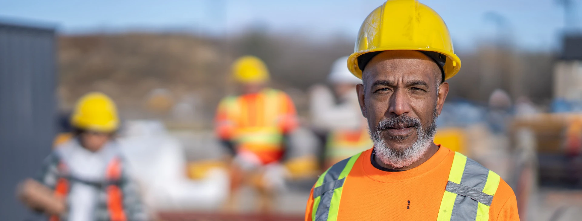 Construction workers wearing safety gear, including helmets and reflective vests, working on an outdoor building site.