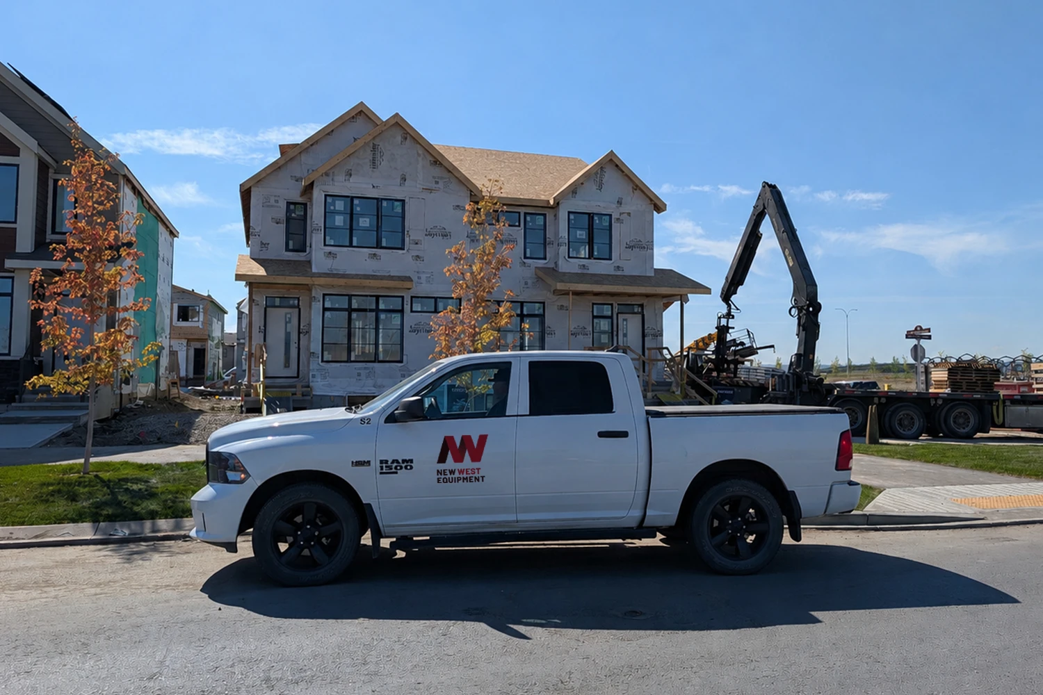 White pickup truck with a construction company logo parked in front of a two-story house under construction on a sunny day.