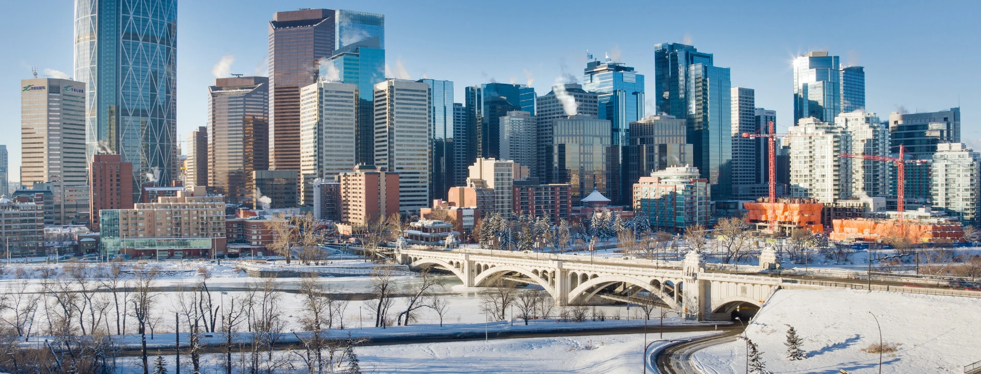 City skyline with modern skyscrapers and bridges over a river during winter, showcasing urban architecture and a snowy landscape.