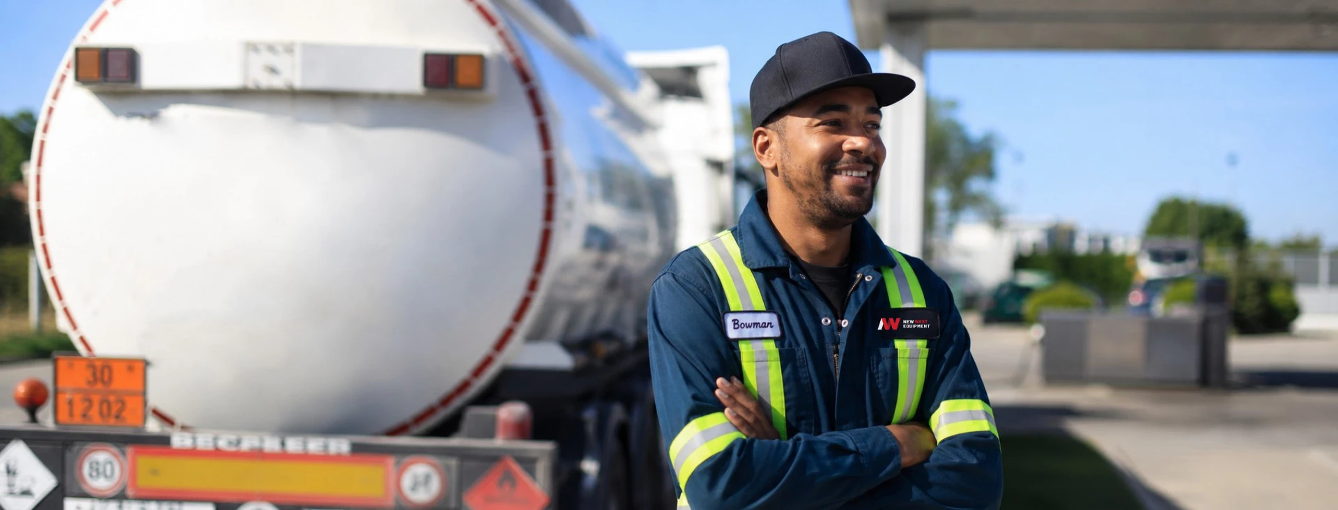 Smiling tanker truck driver in safety gear standing outdoors near the vehicle on a sunny day.