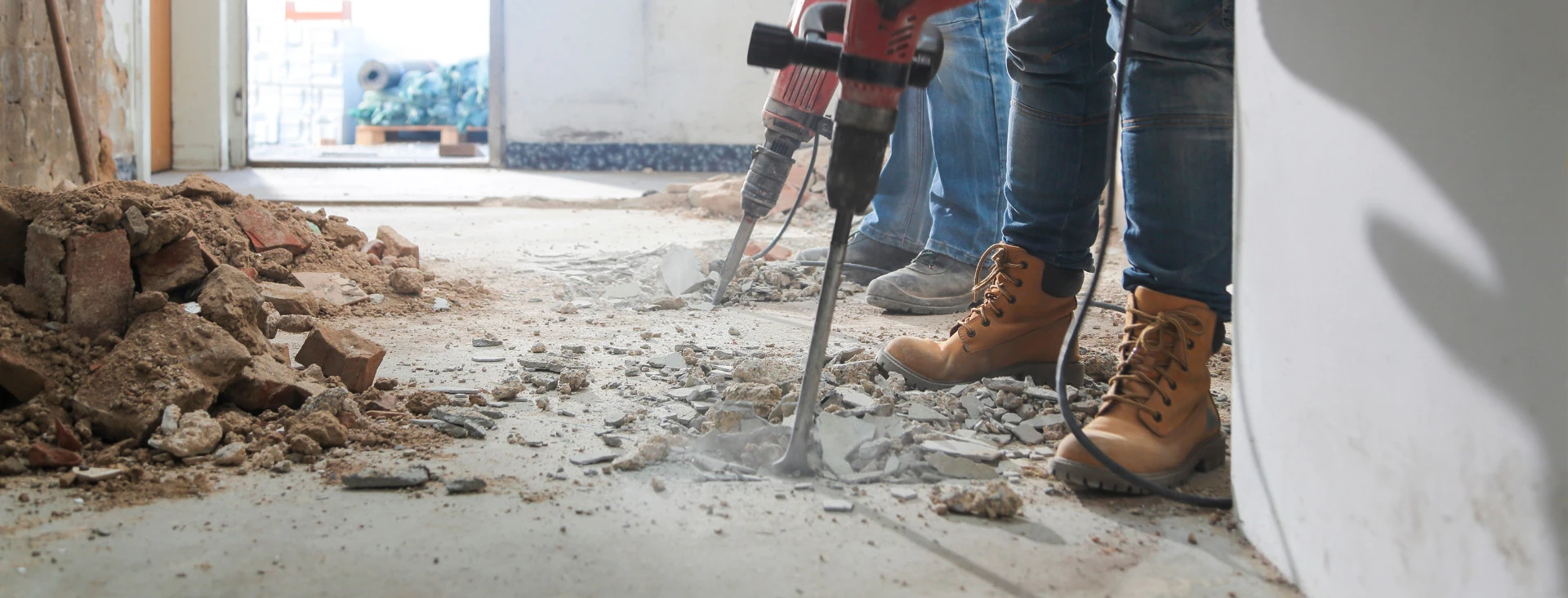 Construction worker using a jackhammer to break up concrete floor during building renovation.