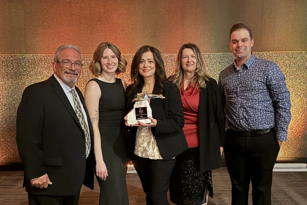 A group of five professionally dressed individuals posing indoors, with one woman holding a trophy or award.