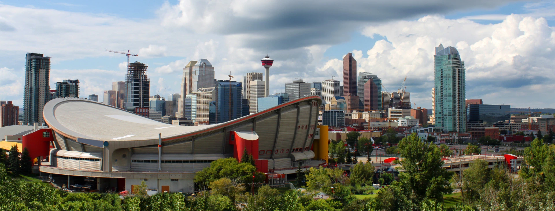 Panoramic view of a modern city skyline with high-rise buildings and a distinctive stadium in the foreground under a partly cloudy sky.